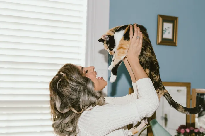 Woman joyfully holding her calico cat in the air